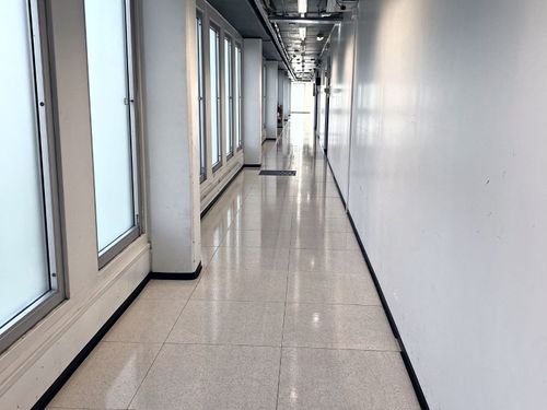 En lang, smal korridor med polert gulv og hvite vegger, foret med store vinduer på venstre side, som leder til et forsvinningspunkt i enden i et av Aurskog Bygg & Renhold Oppskuring/beningsbedriftsområder.