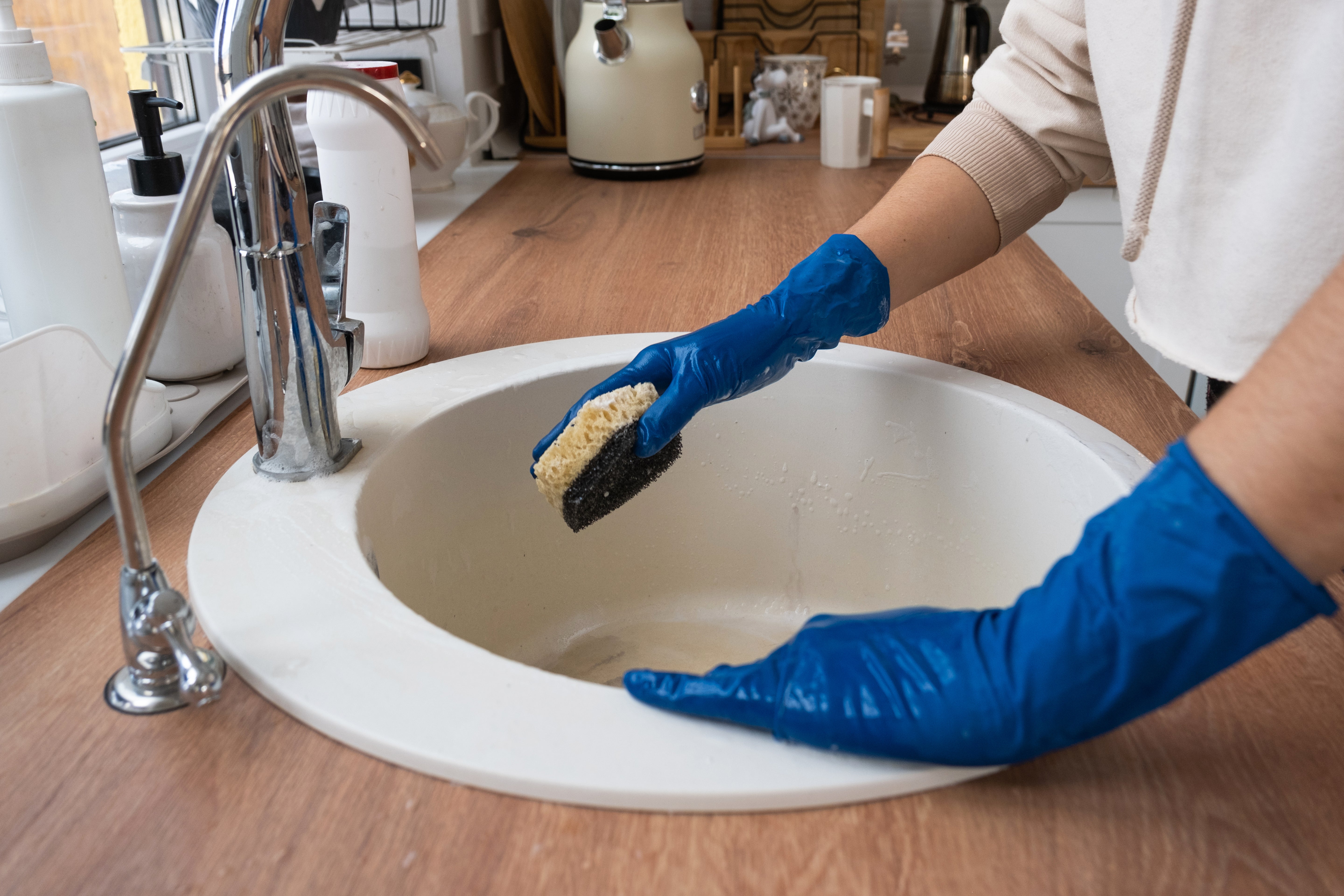 En person iført blå hansker som vasker en vask under Aurskog Bygg & Renhold vårrengjøring.